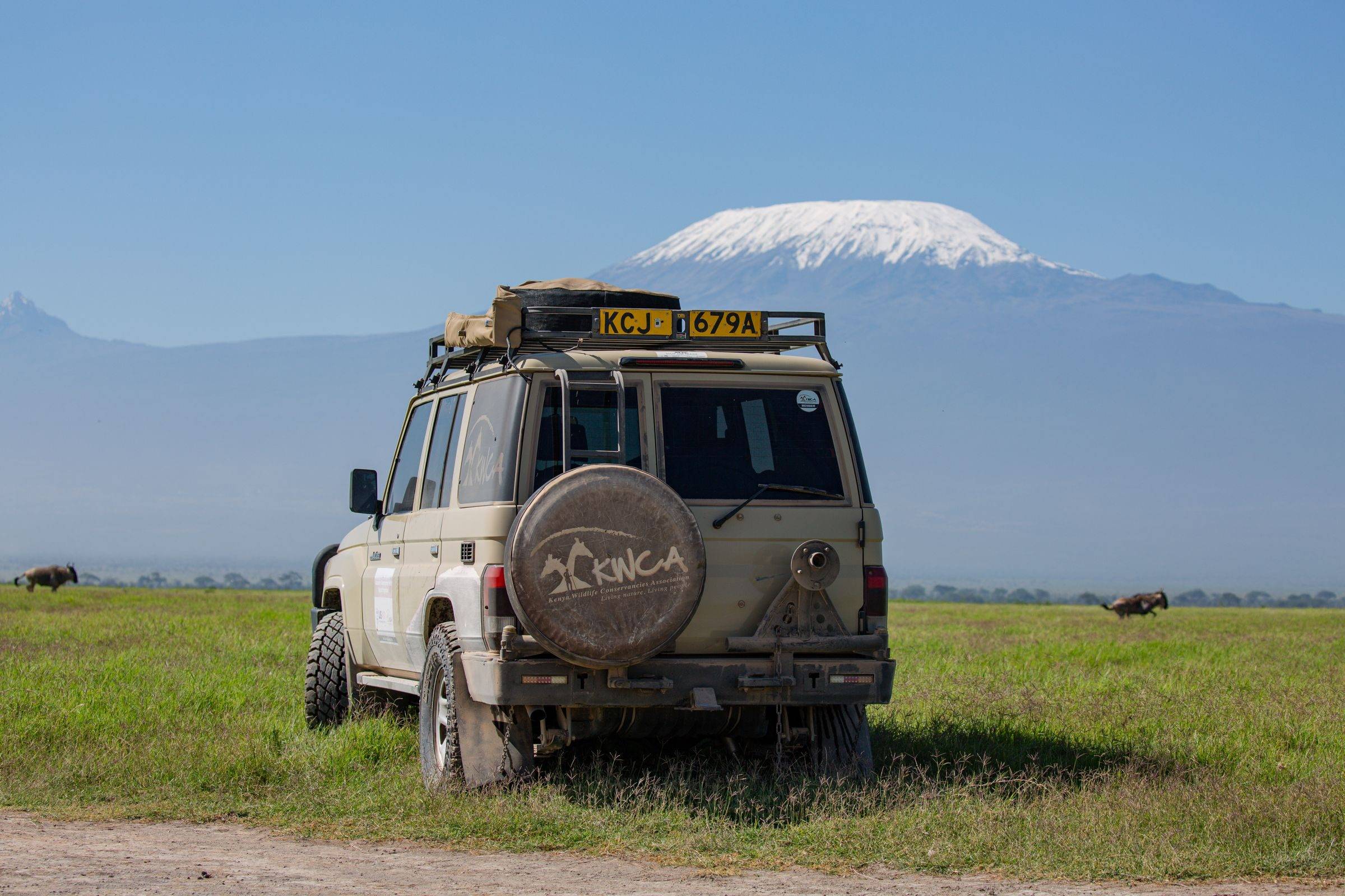 A Land Cruiser safari vehicle on the grassland with Kilimanjaro behind